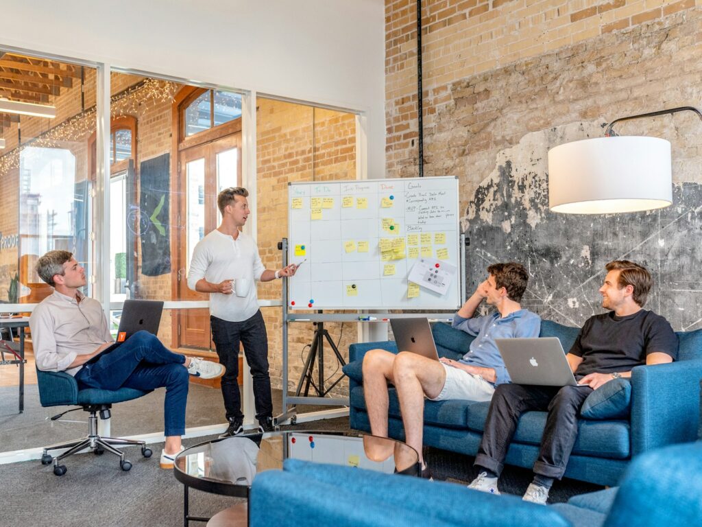 three men sitting while using laptops and watching man beside whiteboard sostenibilità aziendale