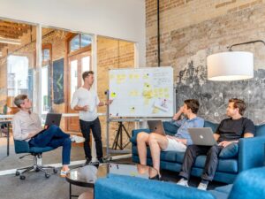 three men sitting while using laptops and watching man beside whiteboard sostenibilità aziendale